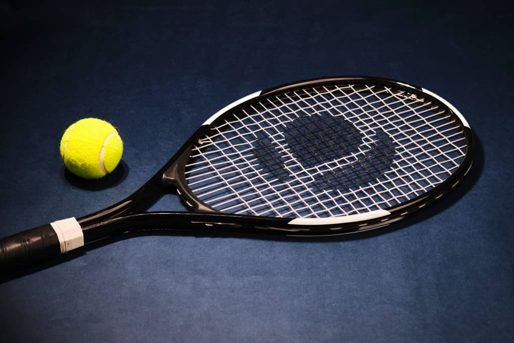 A product image of a black tennis racket and a ball on a blue background.